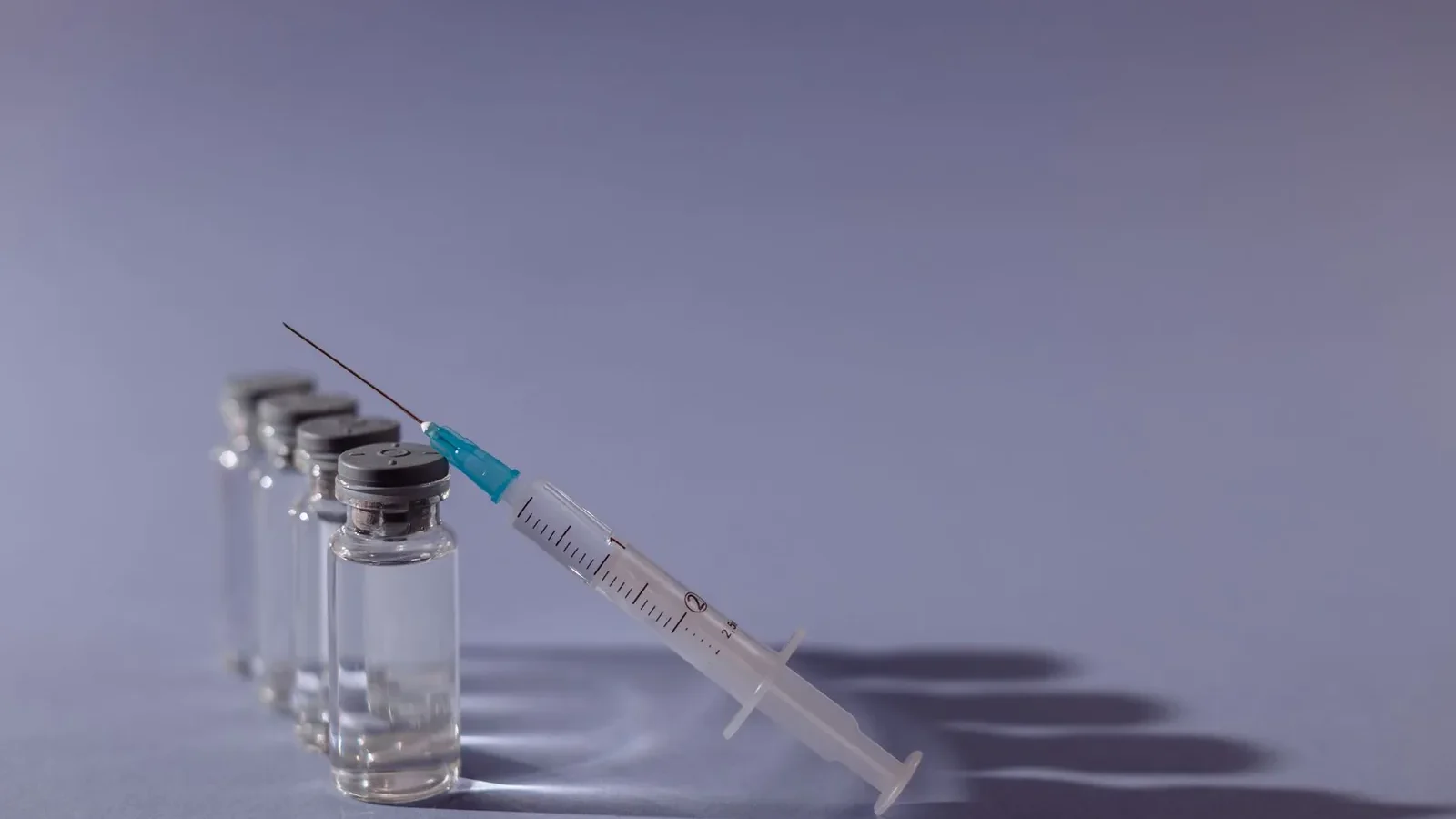 Syringe and vaccine vials arranged on gray surface, symbolizing healthcare and immunization.