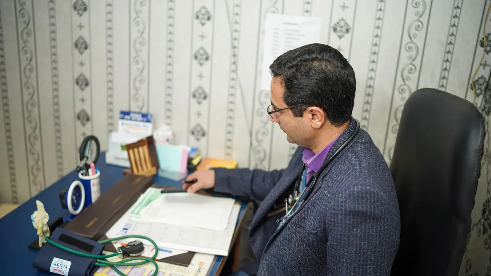 Doctor reviewing medical documents at desk in clinic office.