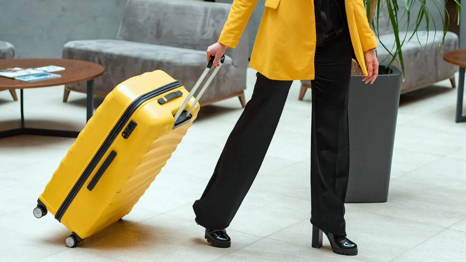 Stylish woman walking in hotel lobby pulling a bright yellow suitcase.