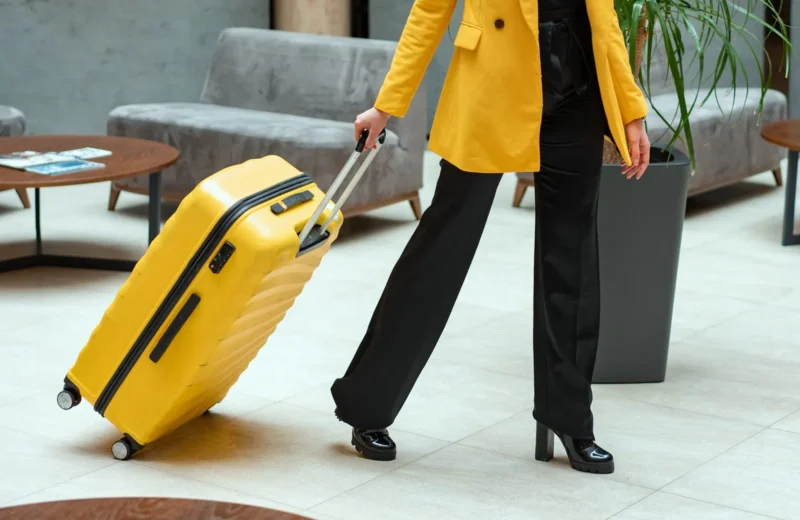 Stylish woman walking in hotel lobby pulling a bright yellow suitcase.