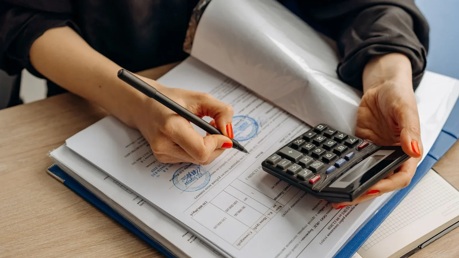 An accountant using a calculator and signing paperwork, showcasing financial analysis.