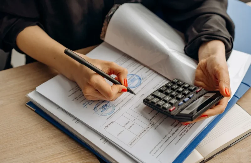 An accountant using a calculator and signing paperwork, showcasing financial analysis.