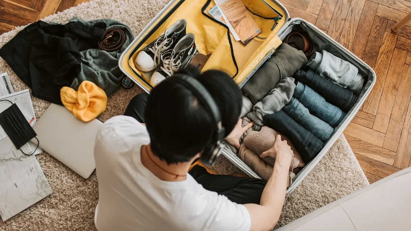 Adult packing clothes in a suitcase while listening to music at home. Overhead view on rug.