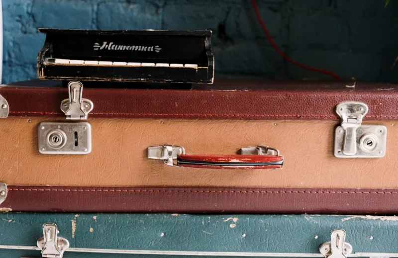 Stack of vintage suitcases topped with an antique harmonium music box against a brick wall.