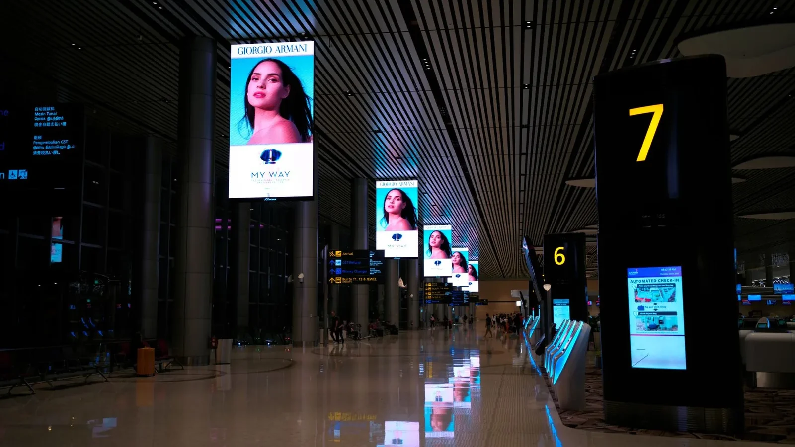 Empty airport hallway with digital displays and glossy floors at night.