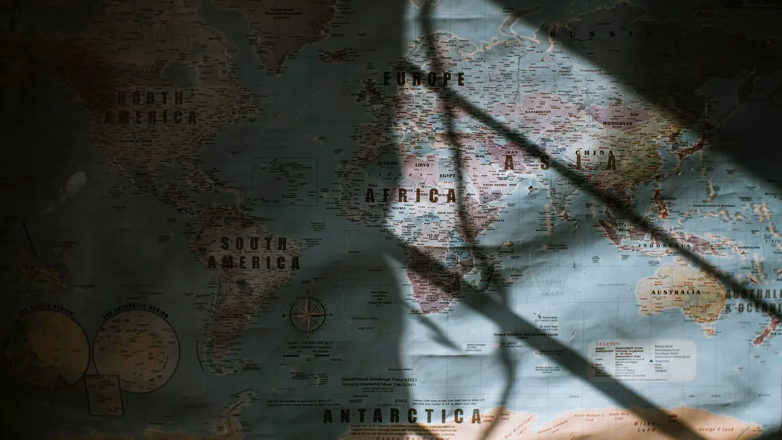 Aged world map with continents and oceans hanging on wall lit with sun.