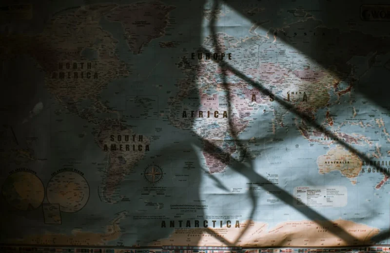 Aged world map with continents and oceans hanging on wall lit with sun.