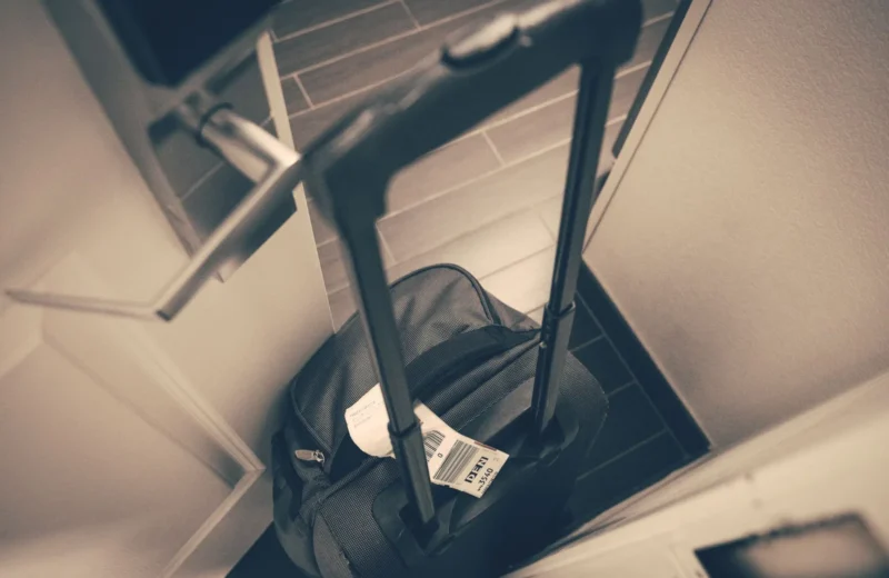 Travel suitcase with tag by hotel door, symbolizing travel or business trip.