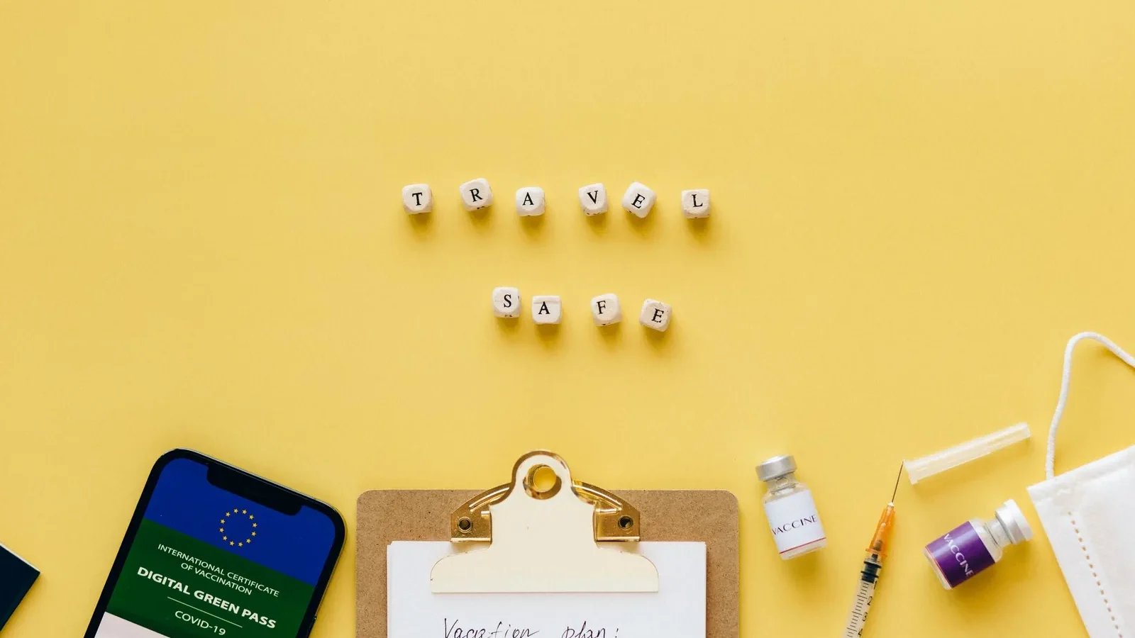 Flat lay showing travel safety essentials like a digital green pass, vaccine, and mask.