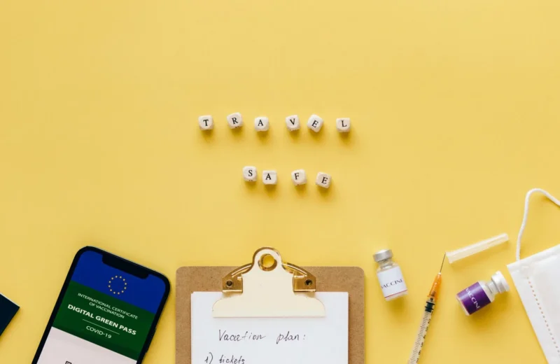 Flat lay showing travel safety essentials like a digital green pass, vaccine, and mask.
