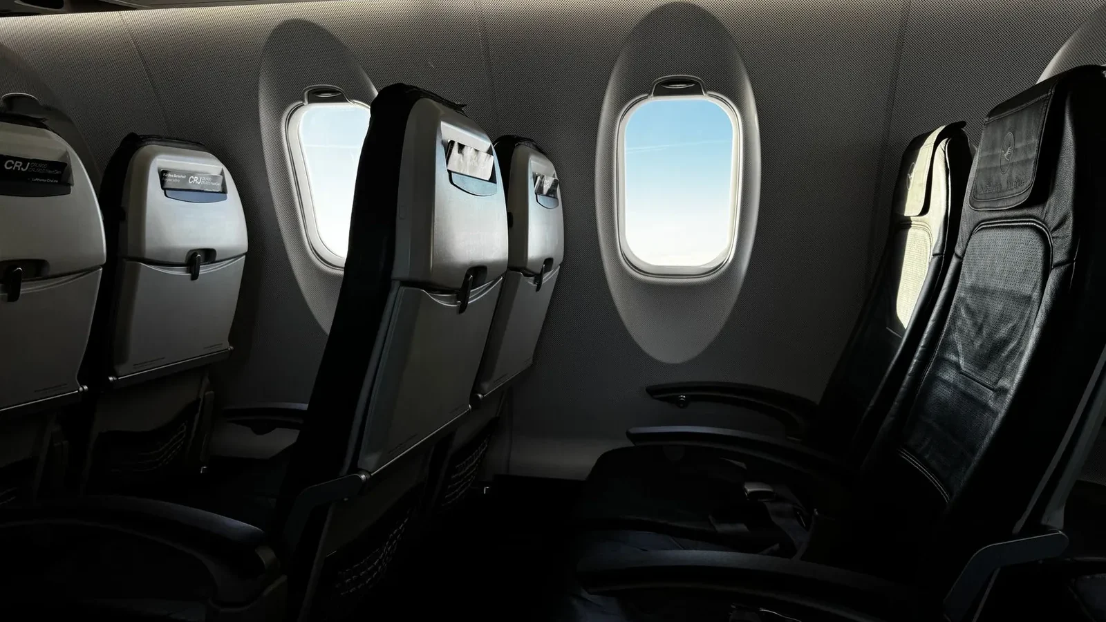 Interior of an empty airplane cabin with a bright sky visible through the window.