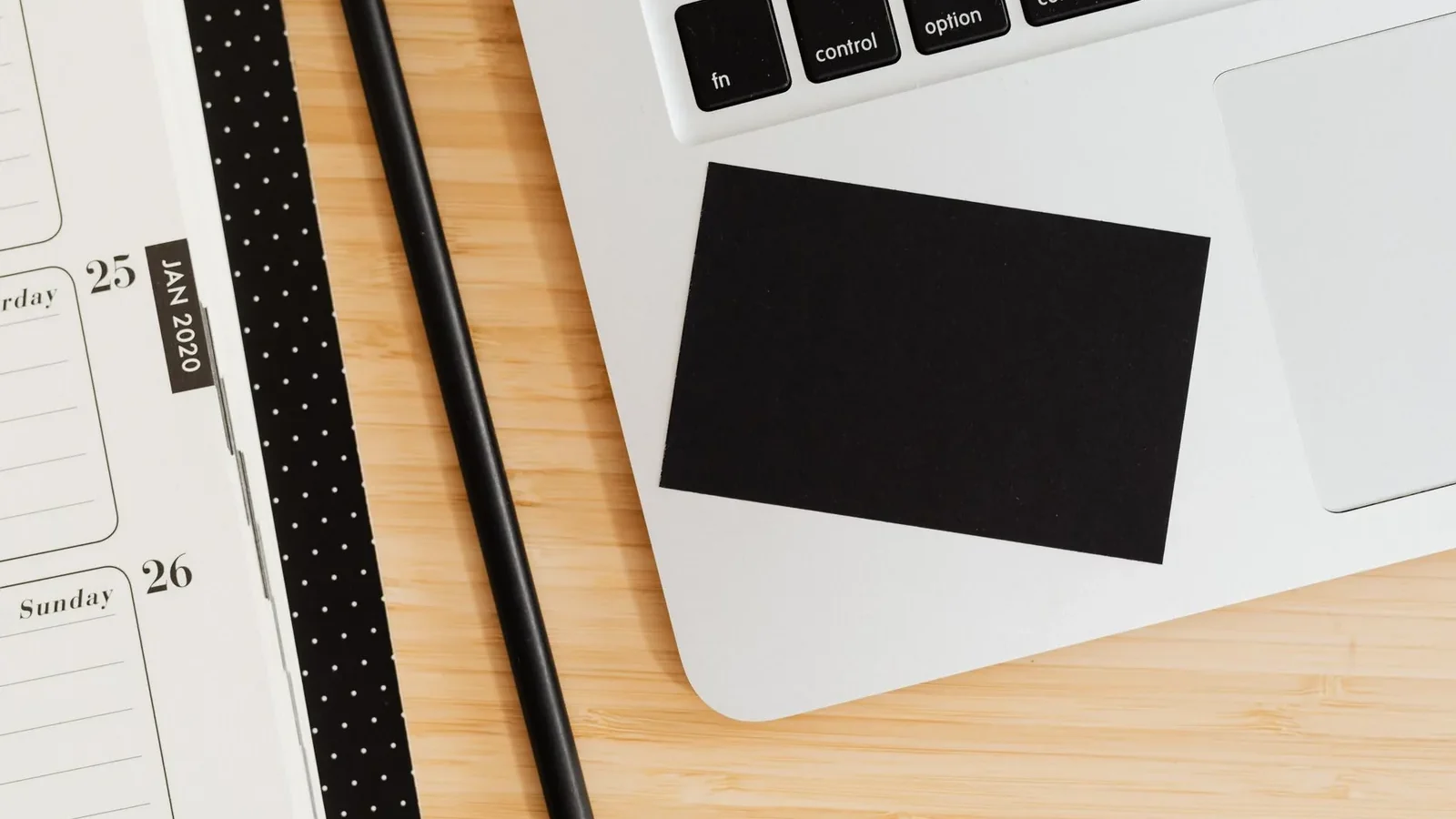 A clean office desk setup with a laptop, notebook, pen, and business card on a wooden surface.