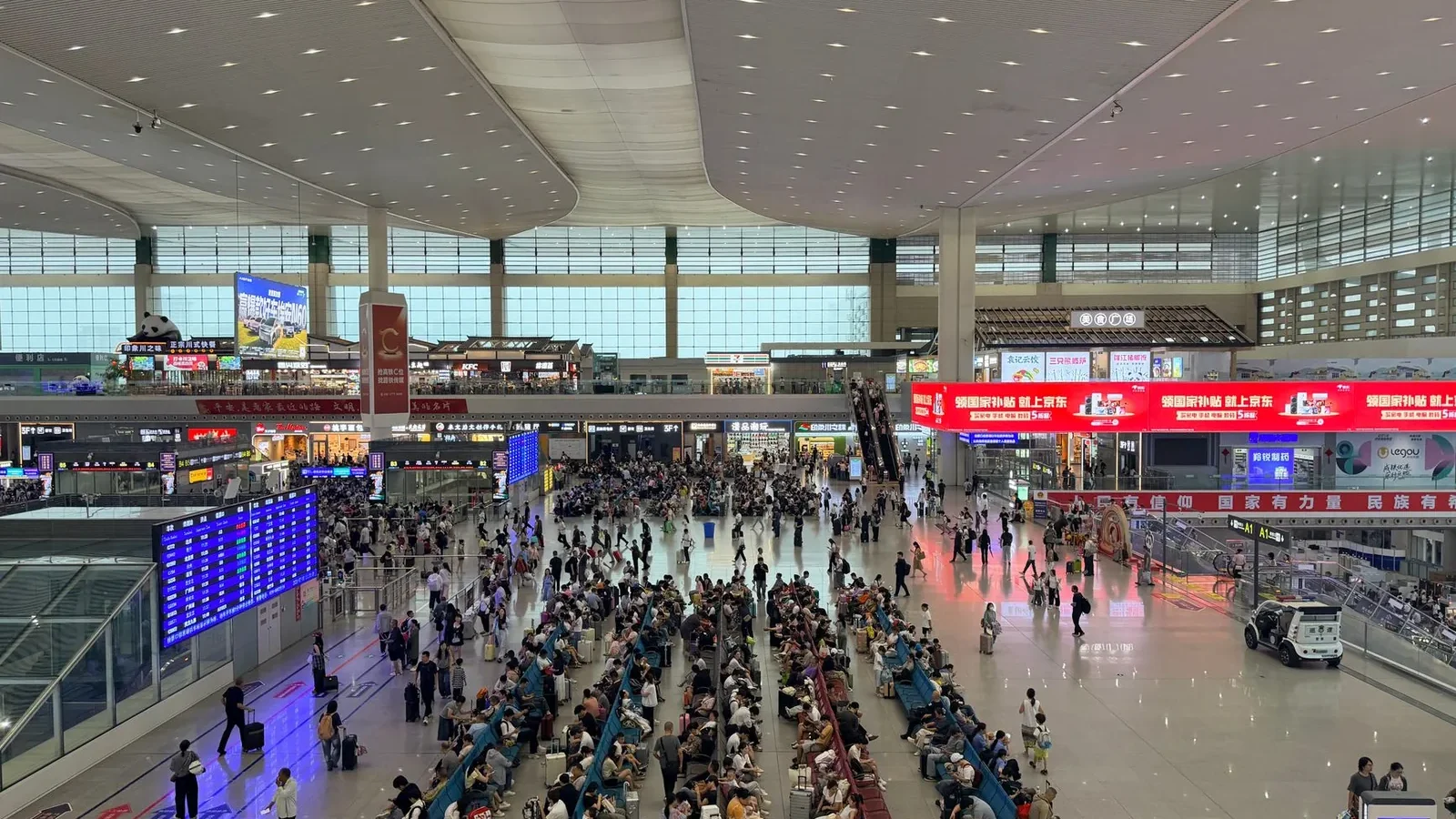 A bustling scene inside Chengdu East Railway Station with crowds and signage.