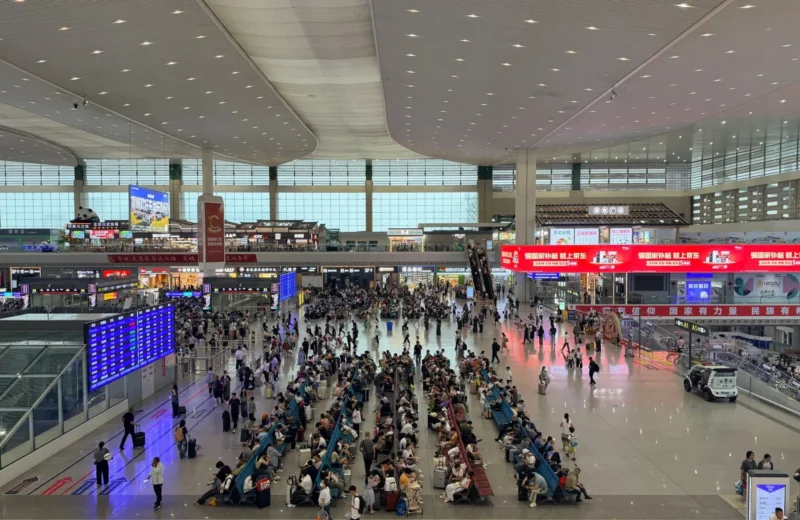 A bustling scene inside Chengdu East Railway Station with crowds and signage.